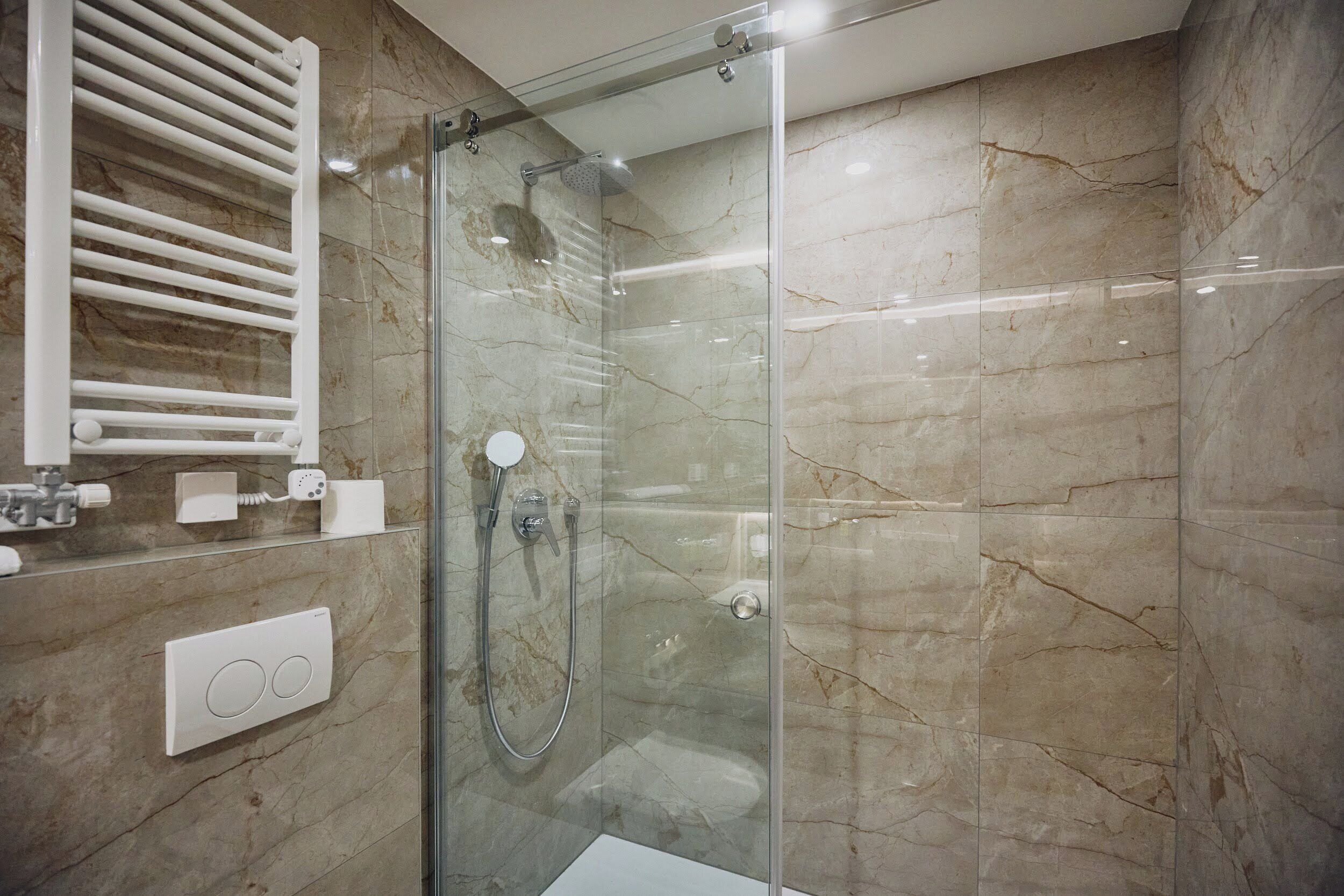 Un baño moderno con ducha de vidrio, paredes de mármol y un perchero blanco.