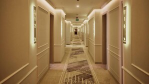 A hotel hallway with numbered doors, recessed lighting, and patterned carpet.