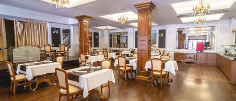Un comedor con varias mesas y sillas, candelabros y piso de madera.