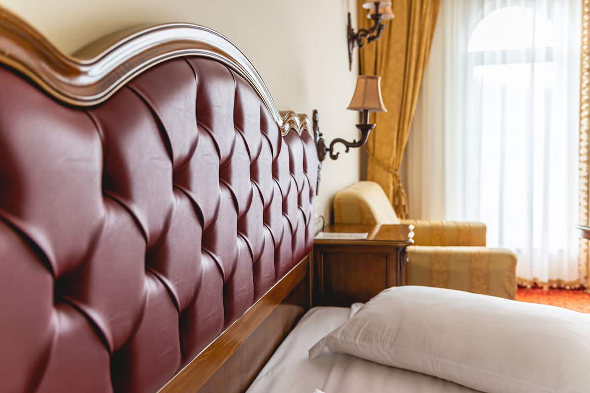 Una habitación de hotel con un cabecero capitonado, una mesita de noche, una lámpara y una silla.
