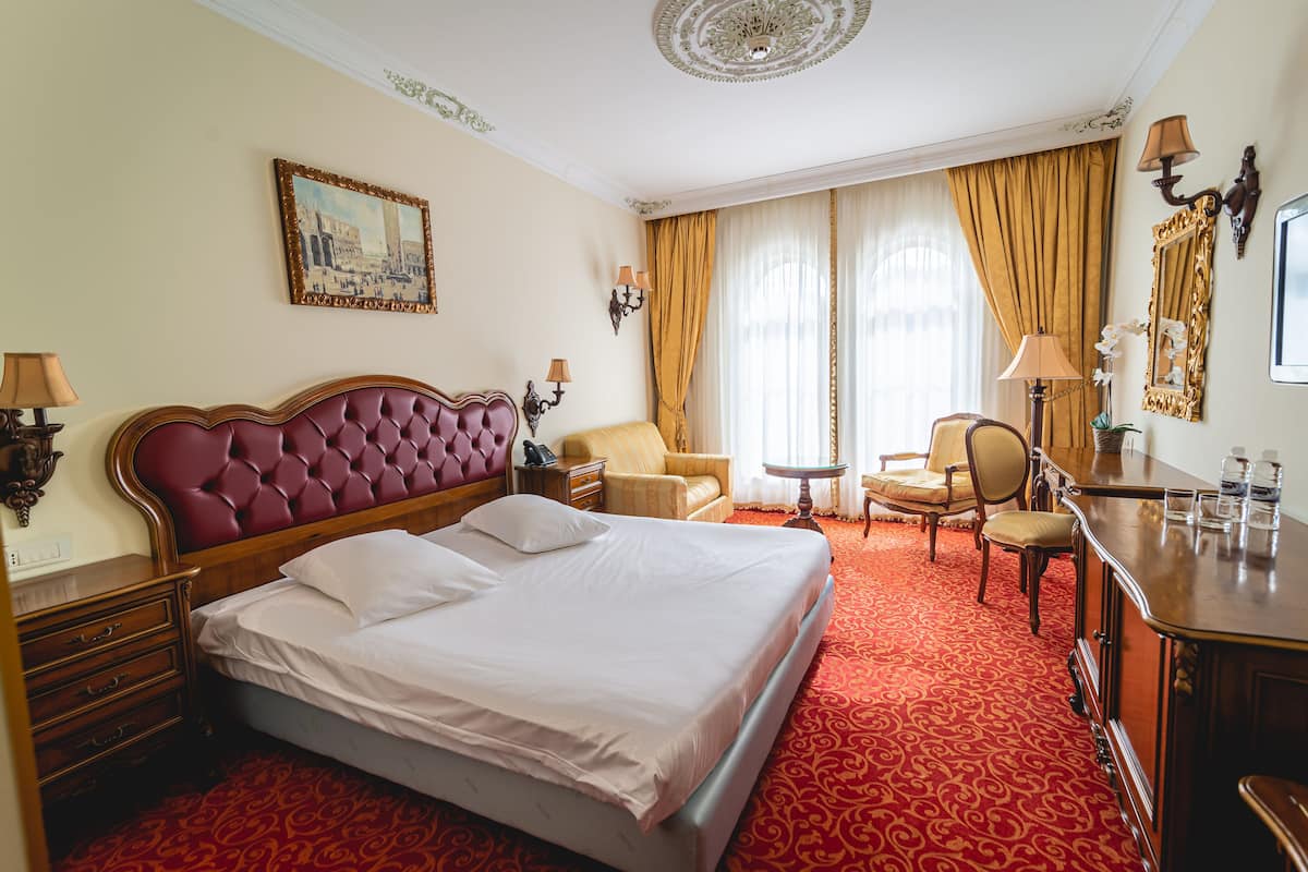 Habitación de hotel con una cama grande, dos sillones, una mesita, un escritorio con lámpara y un espejo.