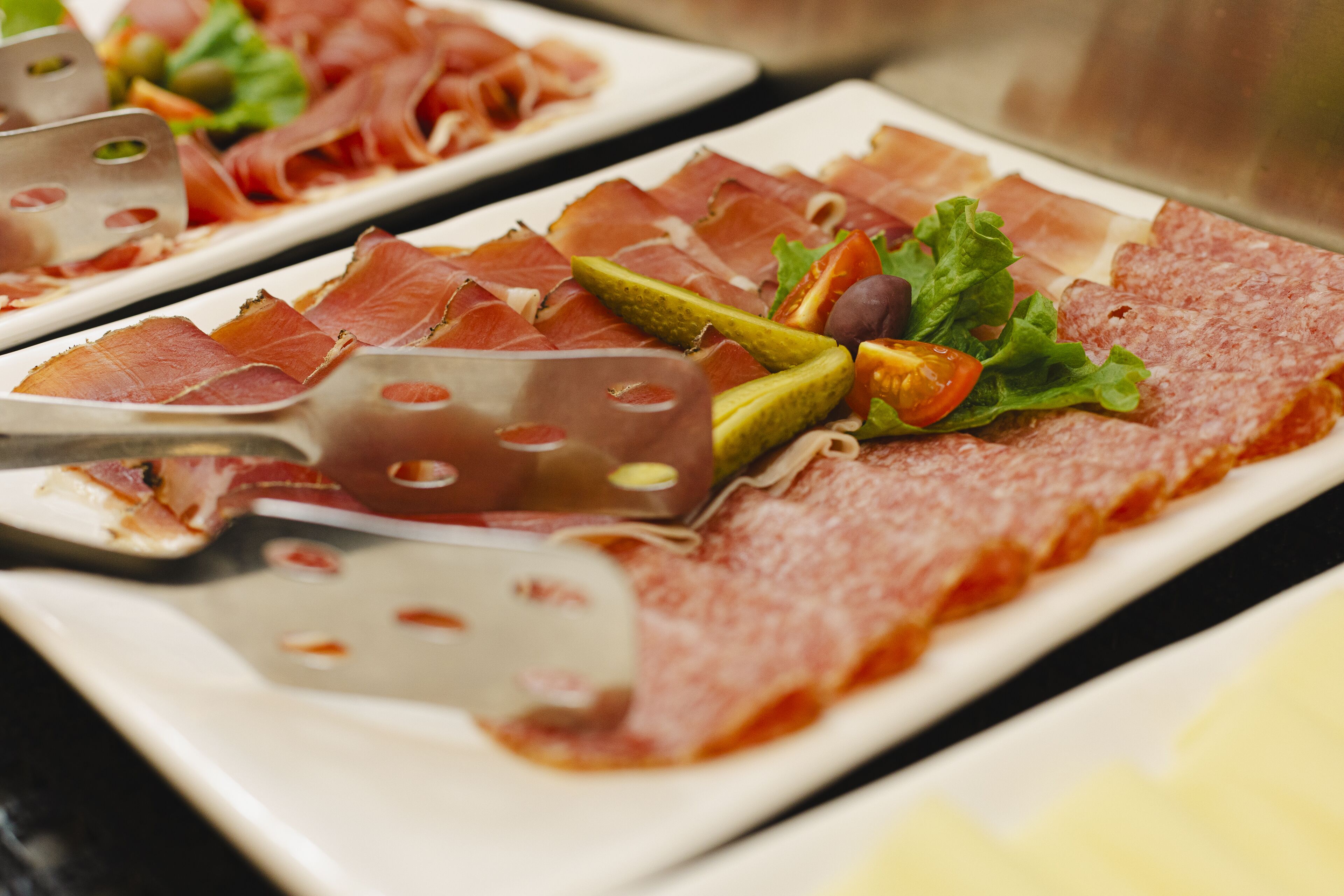 A platter of sliced meats with a knife and some vegetables.