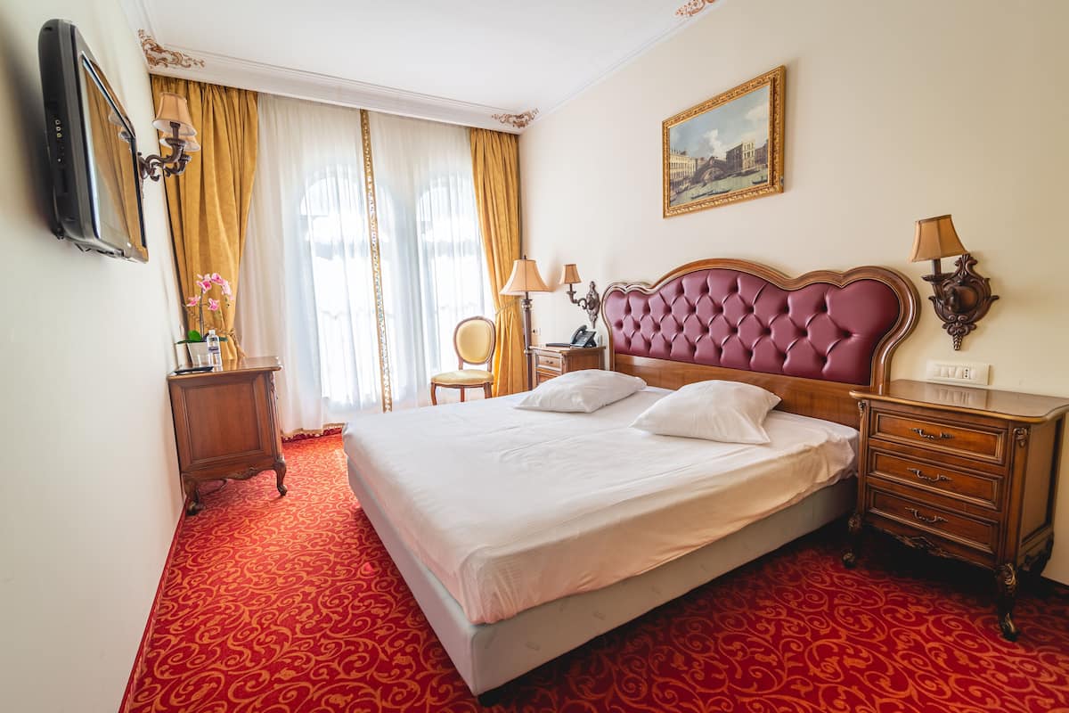Una habitación de hotel con una cama grande, una mesita de noche de madera, una silla y un escritorio con una lámpara.