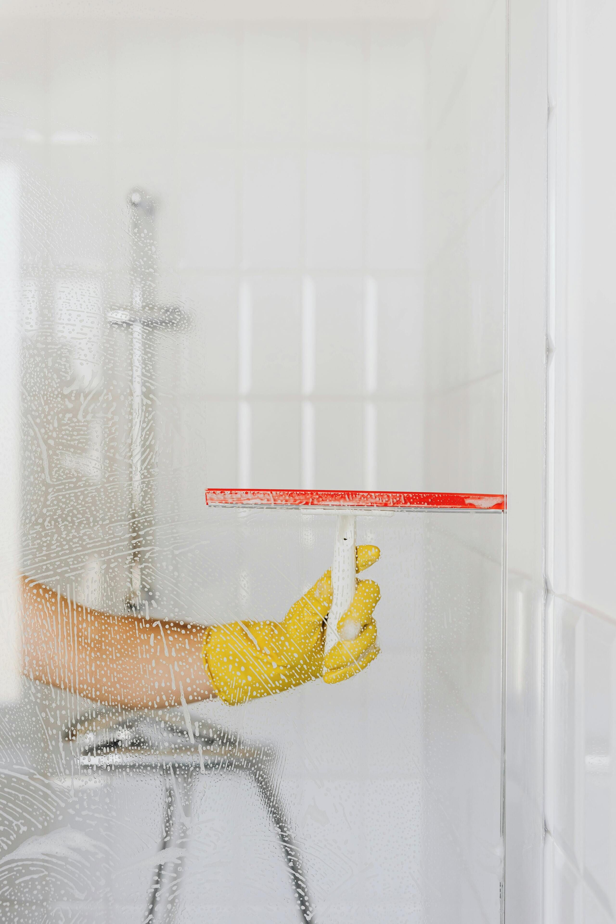 A hand holding a red ruler against a frosted glass shower door.
