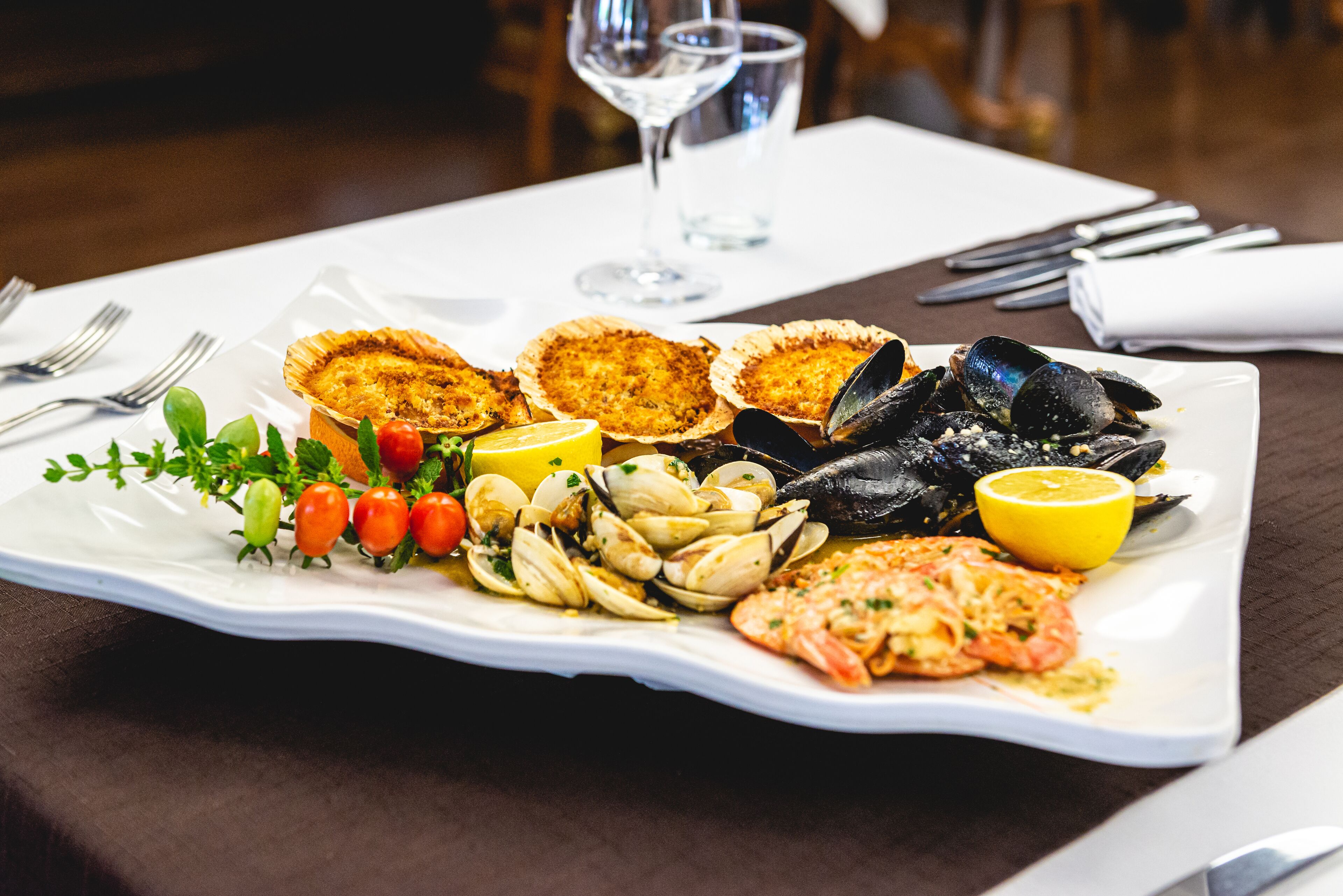 Una bandeja de mariscos con mejillones, almejas, camarones y un gajo de limón sobre un plato blanco.