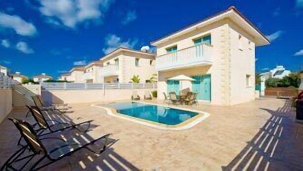 A residential building with a swimming pool, sun loungers, and a clear blue sky.