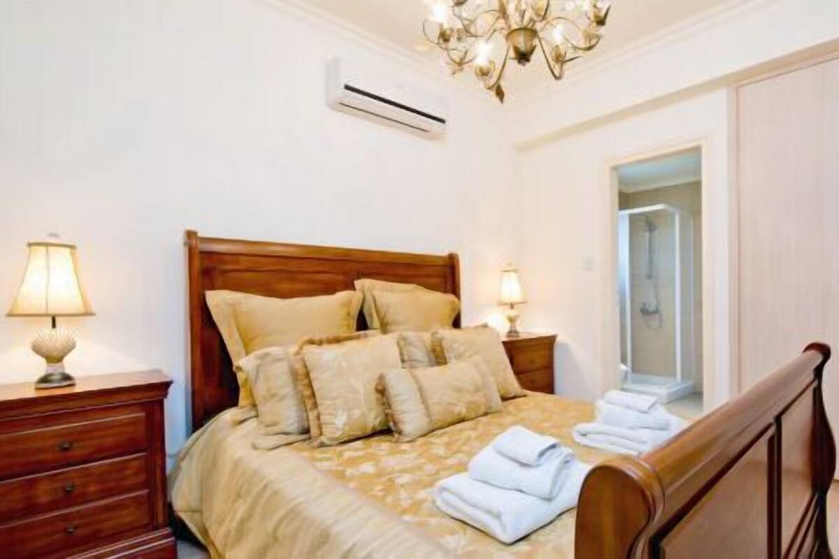 Une chambre à coucher avec un lit en bois, deux tables de chevet avec des lampes, un lustre, un appareil de climatisation et une armoire.