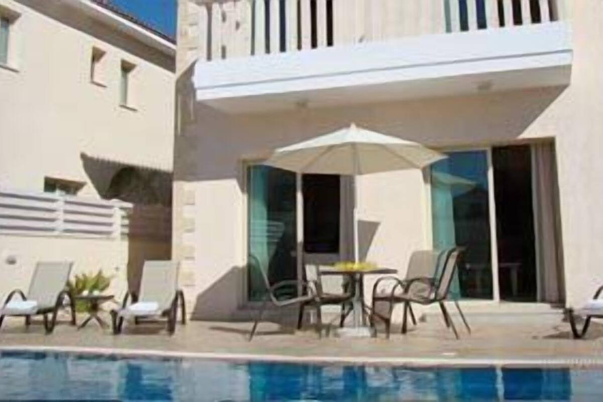 Un hôtel moderne doté d’un espace piscine, comprenant des chaises longues et une table avec des parasols.