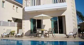 Een modern hotel met een zwembadgedeelte, inclusief ligbedden en een tafel met parasols.