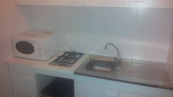 A compact kitchen with white cabinets, a microwave, a gas stove, and a stainless steel sink.