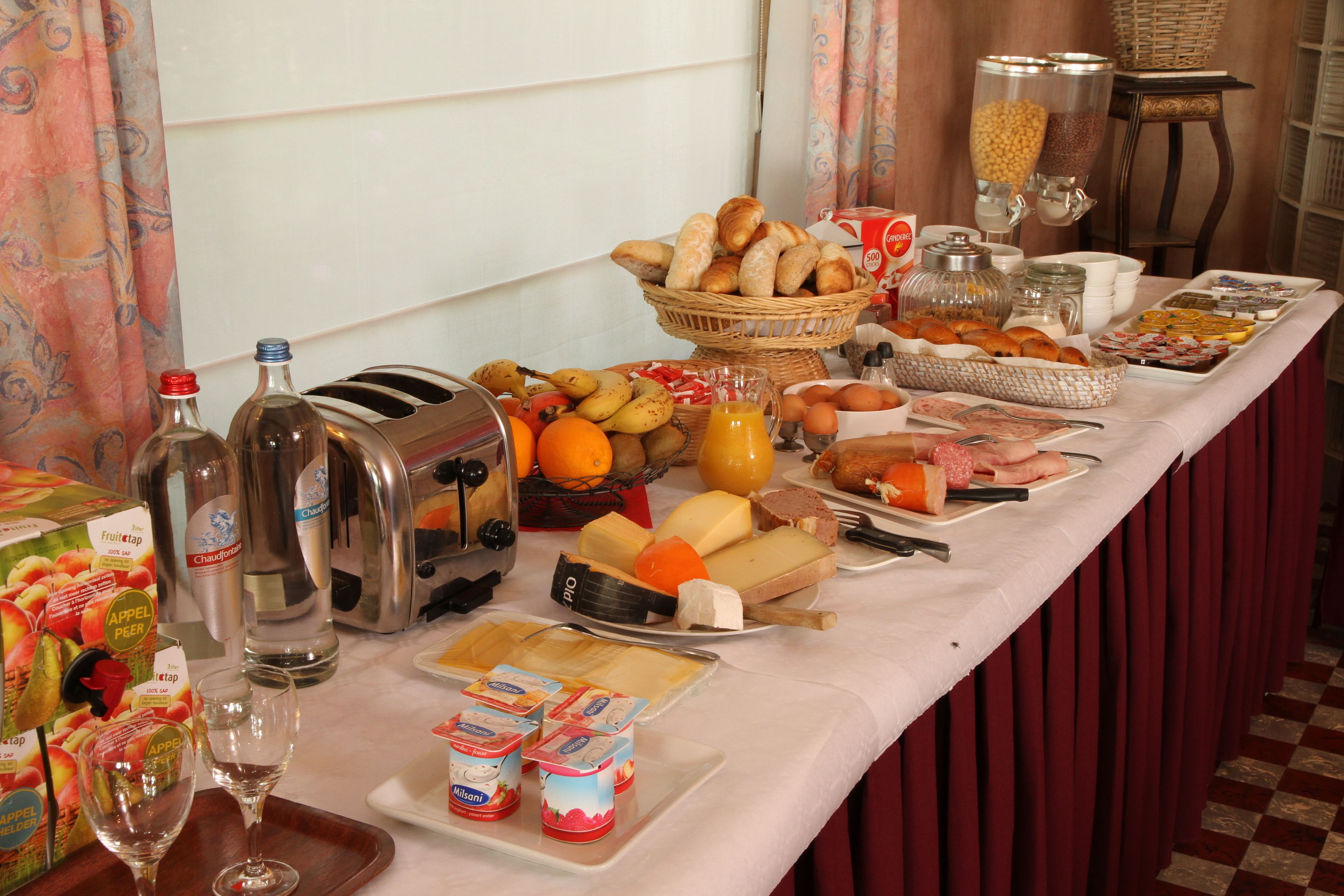 Una mesa de buffet con diversas opciones de comida, entre ellas frutas, quesos y pastelería.