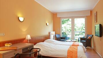 A hotel room with a bed, desk, chair, and a balcony with chairs and a table.
