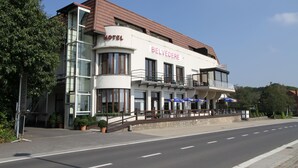 A hotel with a modern design, featuring a prominent balcony and outdoor seating area. - Belvedere (Heuvelland)