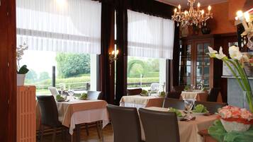 A dining area with tables set for two, chairs, and a chandelier.