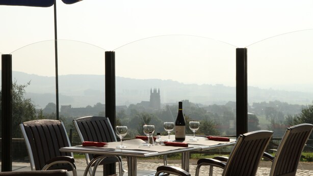 A dining table with chairs, a bottle of wine, and glasses on a terrace overlooking a distant view of a castle. - Belvedere (Heuvelland)
