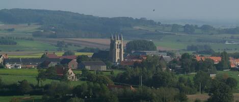 A rural landscape with a prominent church tower, surrounded by fields and residential buildings.