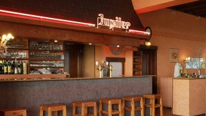 A bar area with wooden stools, a neon sign, and shelves stocked with bottles and glasses. - Belvedere (Heuvelland)