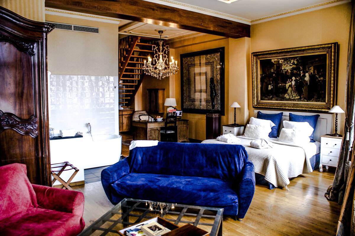 A spacious living room with a large blue sofa, a red armchair, a wooden coffee table, and a chandelier.