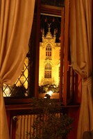 Vista a través de una ventana con cortinas, mostrando un edificio de arquitectura ornamentada y una estatua en la parte superior.