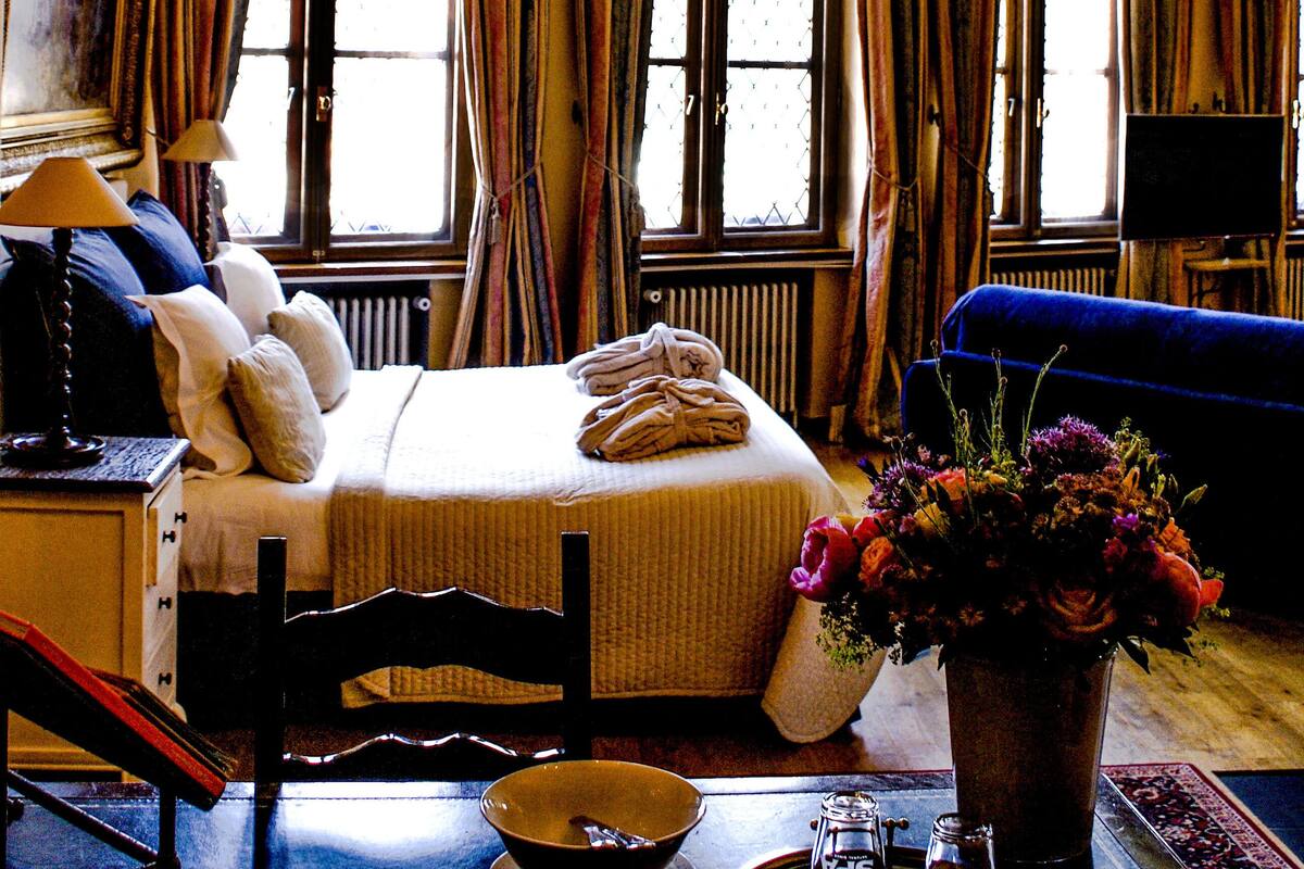 A room with a large chandelier, a bed with pillows, a blue sofa, a vase with flowers, and a tray with salt and pepper shakers.