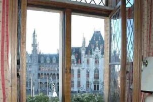 Vista desde una habitación con ventanas amplias que dan a un edificio histórico con múltiples torres y una estatua en primer plano.