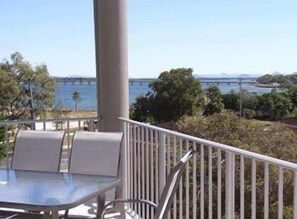 A balcony with a table and chairs, overlooking a body of water and a bridge. - On the Bay Apartments (Bongaree)