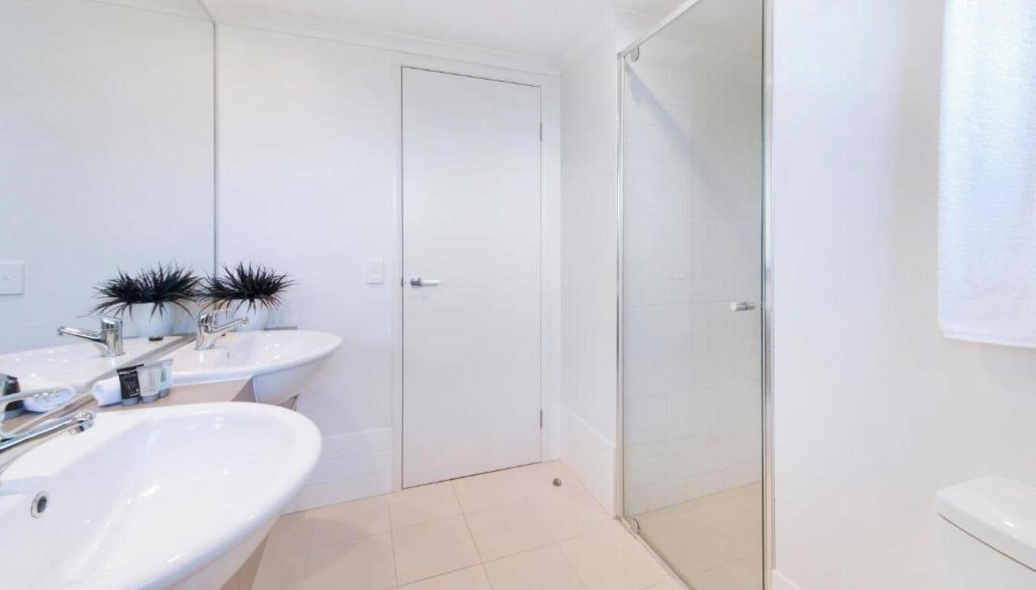 A bathroom with two sinks, a shower, and a toilet.