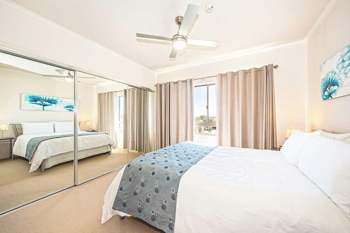 A hotel room with a large bed, a ceiling fan, a mirror, and a view of the outdoors.