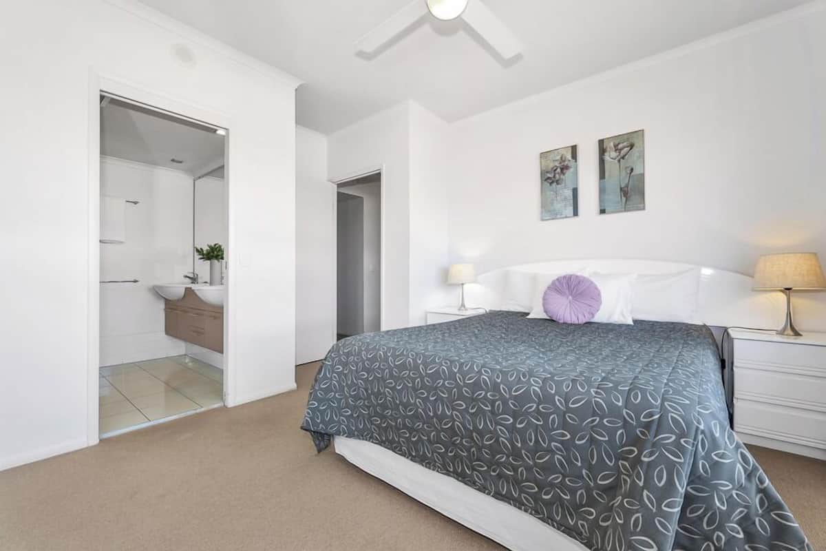 A modern bedroom with a large bed, a bedside table with a lamp, and a bathroom visible through an open door.