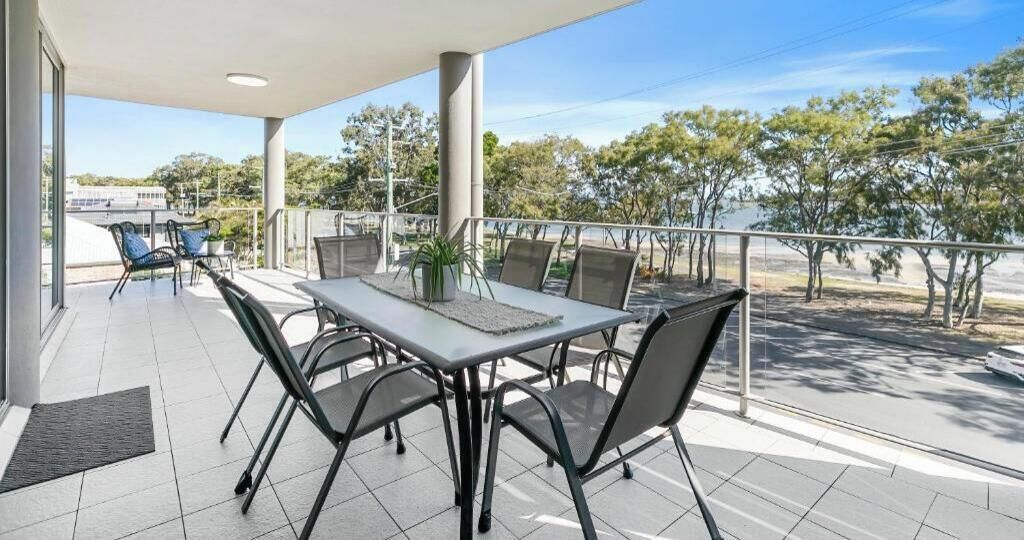 Ein Balkon mit Tisch und Stühlen, Blick auf Bäume und einen klaren Himmel.