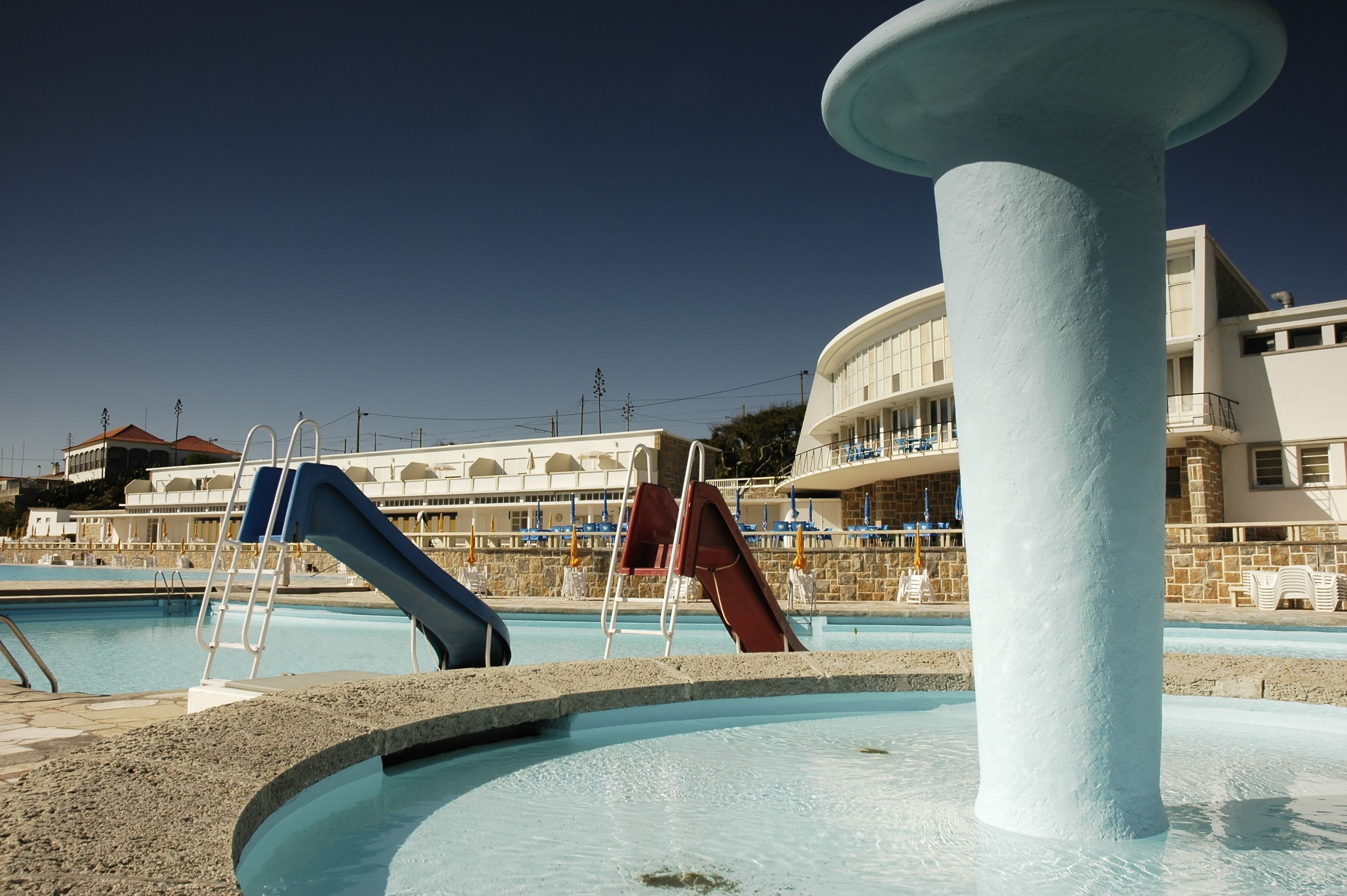 Une piscine avec deux toboggans, une colonne blanche et un bâtiment doté de balcons en arrière-plan.