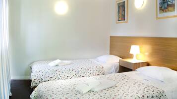 Une chambre d’hôtel avec deux lits, chacun agrémenté de draps et de serviettes à motifs floraux. Une table de chevet avec une lampe se trouve entre les deux lits.