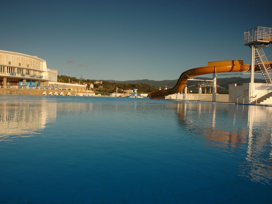 Una piscina con tobogán de agua, una torre de salvavidas y un edificio de fachada curva.