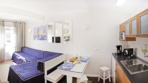 A compact room with a sofa, a dining table with breakfast, a small kitchen area, and a view of the outdoors. - Sintra Sol - Apartamentos Turisticos (Sintra)