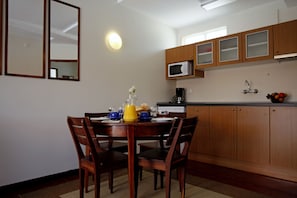 Un comedor con una mesa y sillas de madera, una cocina con armarios de madera, un microondas y un frutero.