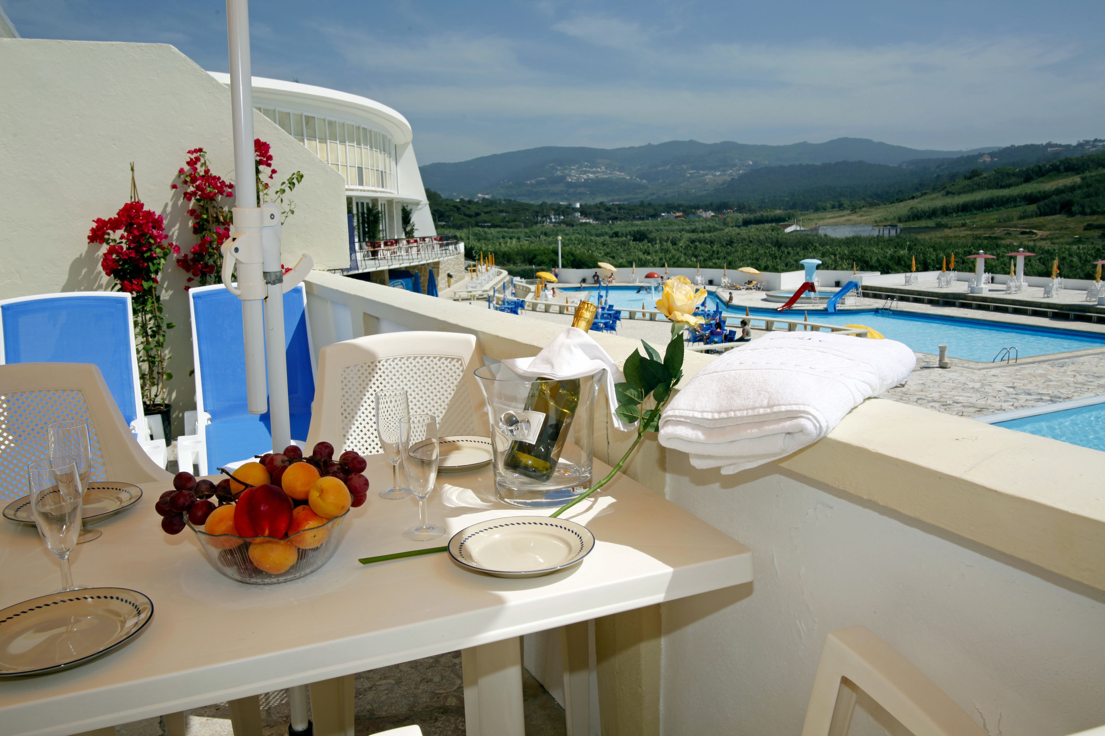 Une table avec des fruits, une bouteille et des verres, donnant sur une piscine et des montagnes.