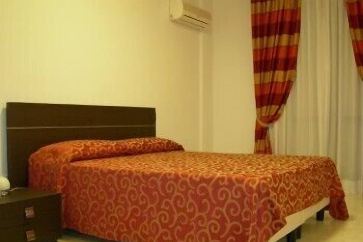 A single bed with a patterned bedspread, a nightstand, and a window with curtains.