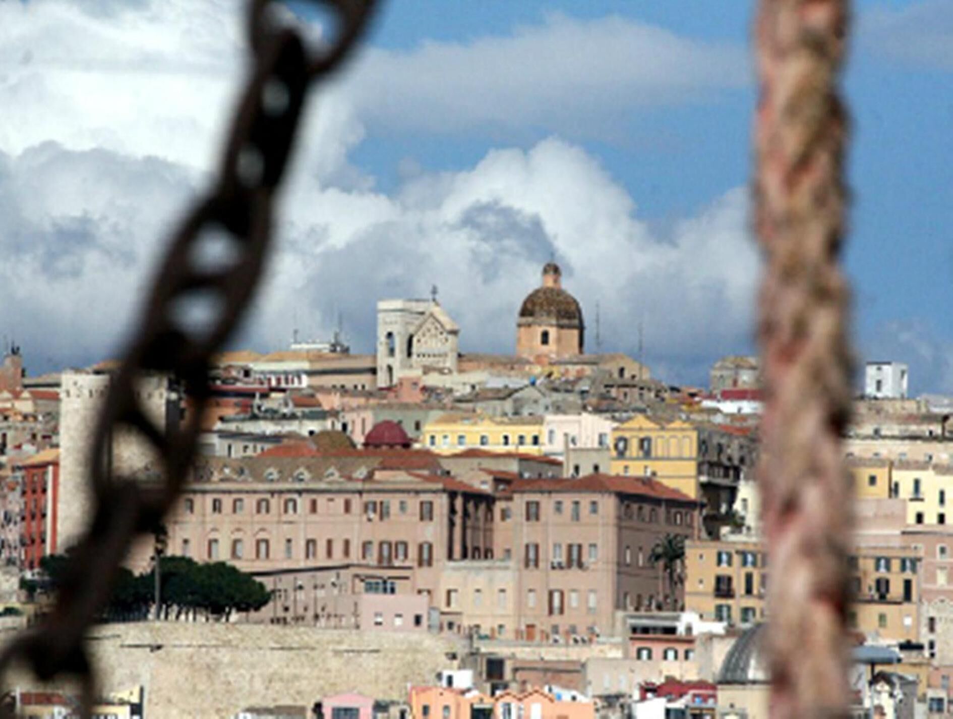 Un paisaje urbano con edificios históricos, una estructura cúpula destacada y una cerca de malla metálica en primer plano.
