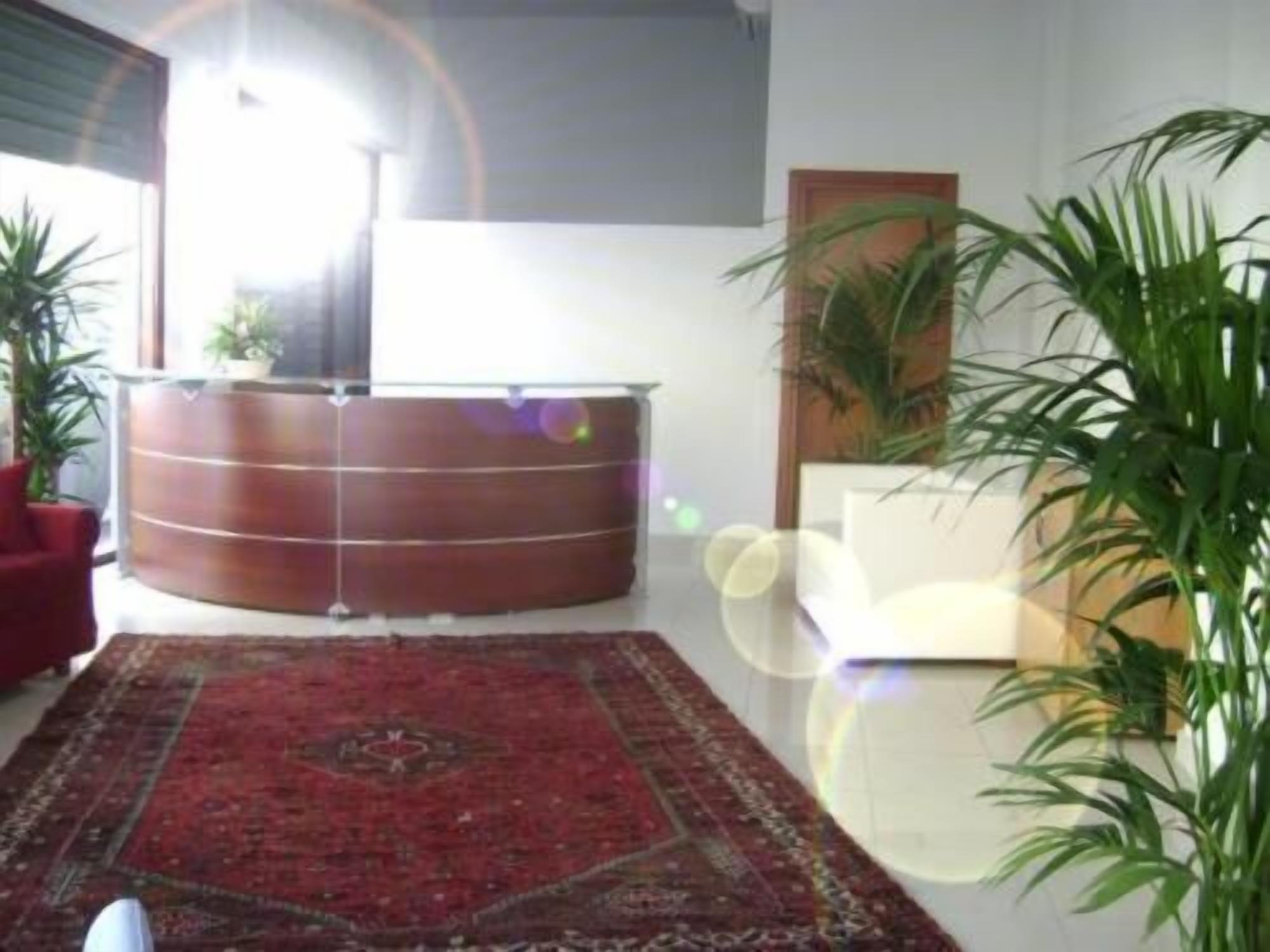 Una habitación con un mostrador de recepción de madera, una alfombra roja estampada y varias plantas en macetas.
