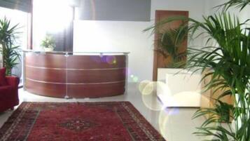 Una habitación con un mostrador de recepción de madera, una alfombra roja estampada y varias plantas en macetas.