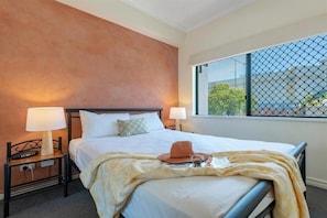 Una camera d'albergo con un letto, due comodini, lampade, una finestra con vista e un cappello sul letto.