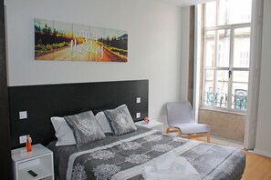 Ein Schlafzimmer mit einem großen Bett, einem Nachttisch, einem Sessel, einem Fenster mit Aussicht und einer Wand mit einem motivierenden Zitat.