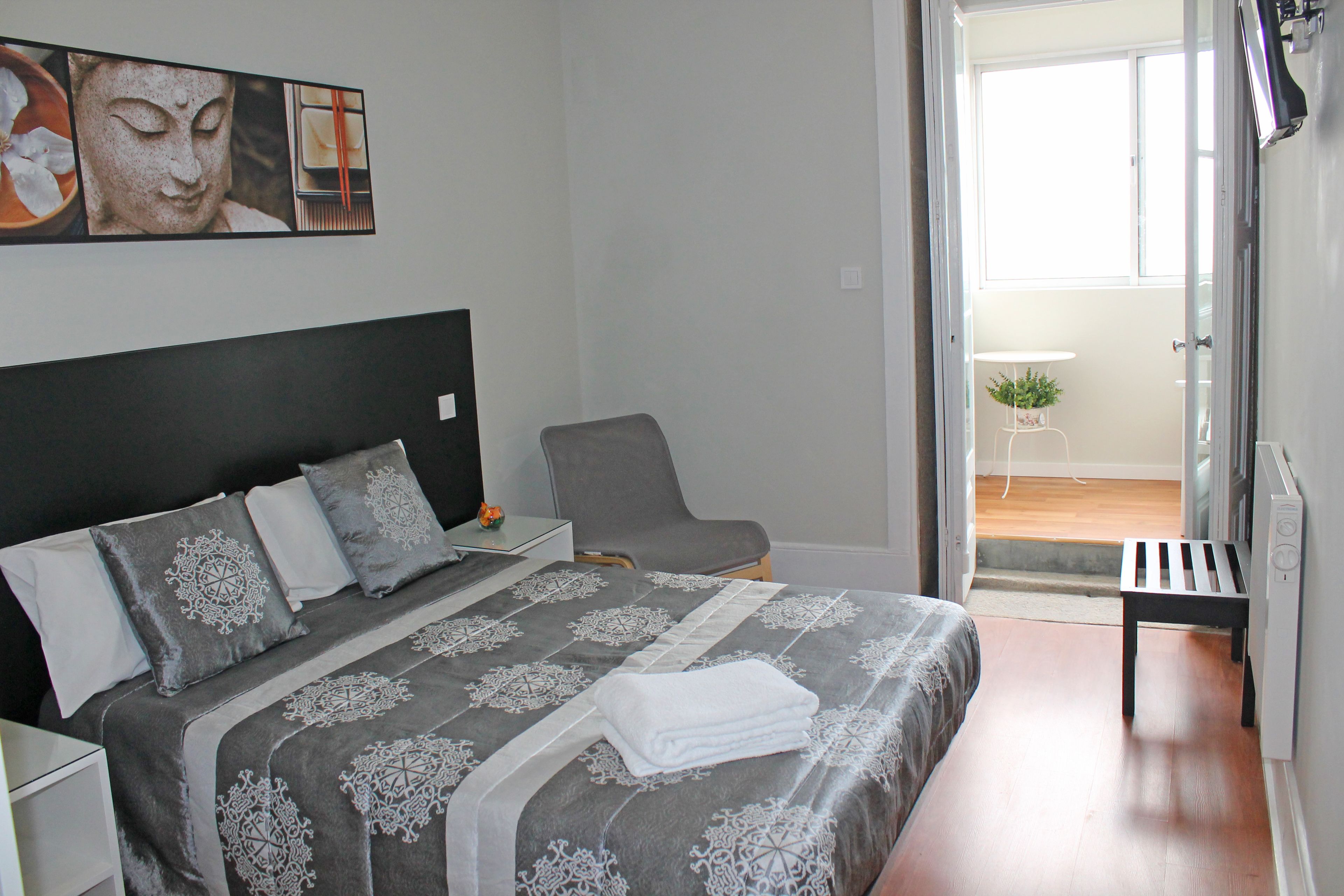 Un dormitorio con cama, una silla, una mesita y una ventana.