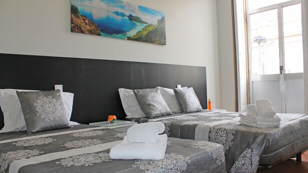 A hotel room with two beds, grey patterned bedspreads, white pillows, and a painting of a coastal landscape on the wall. - Lunar Guest House (Porto)