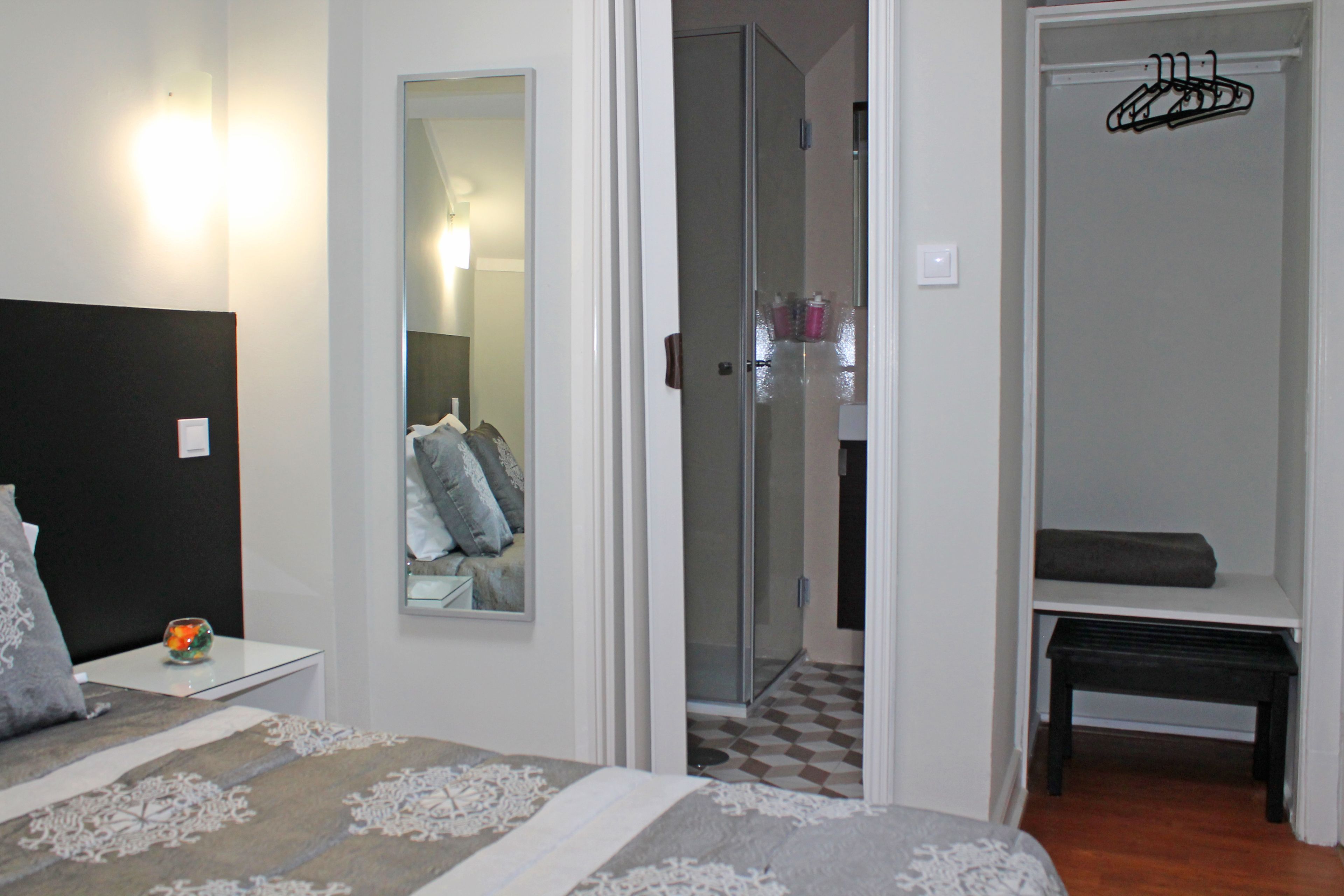 A bedroom with a bed, a bedside table, a mirror, and a closet with a bench.