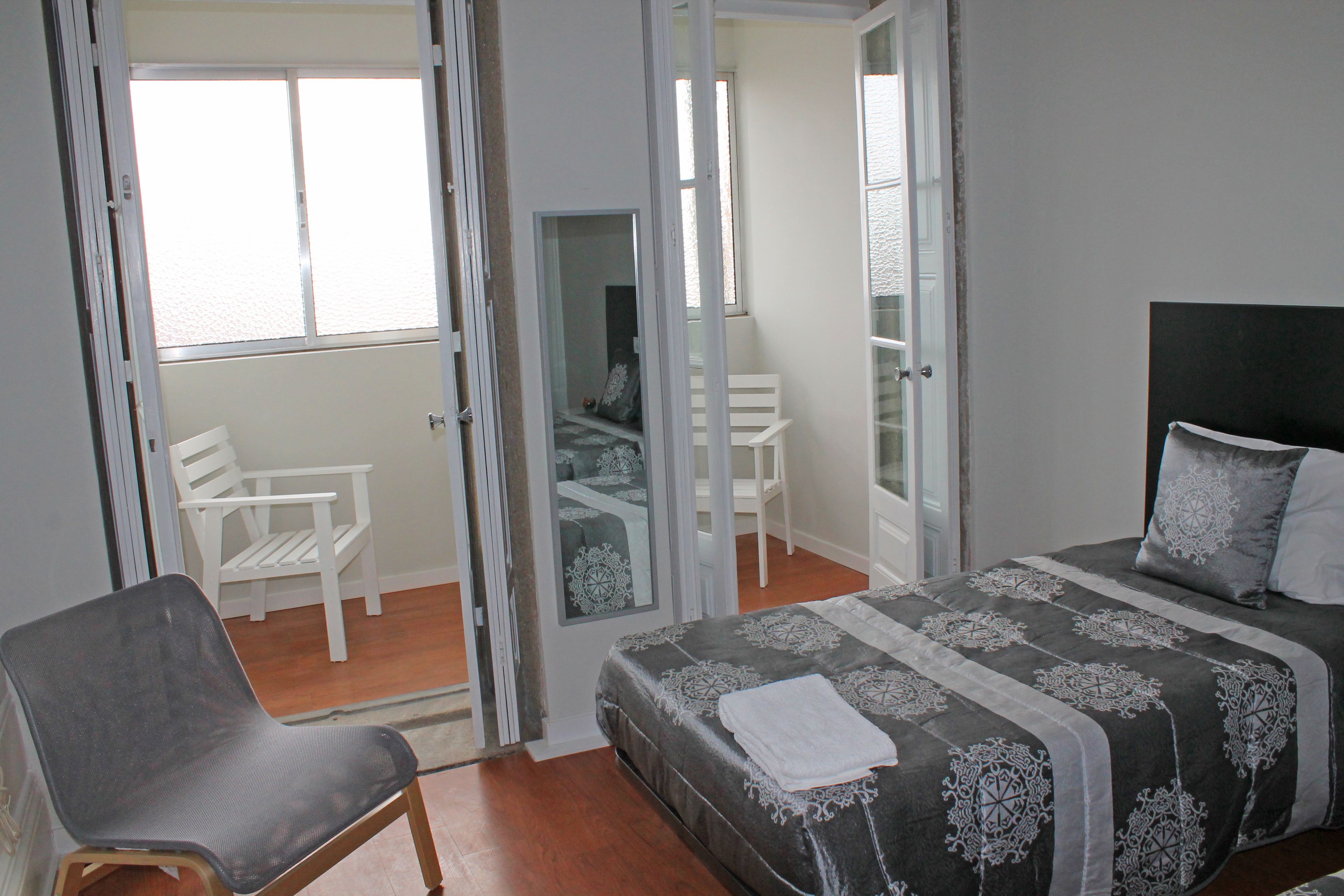 A bedroom with a bed, a chair, and a view through an open door.