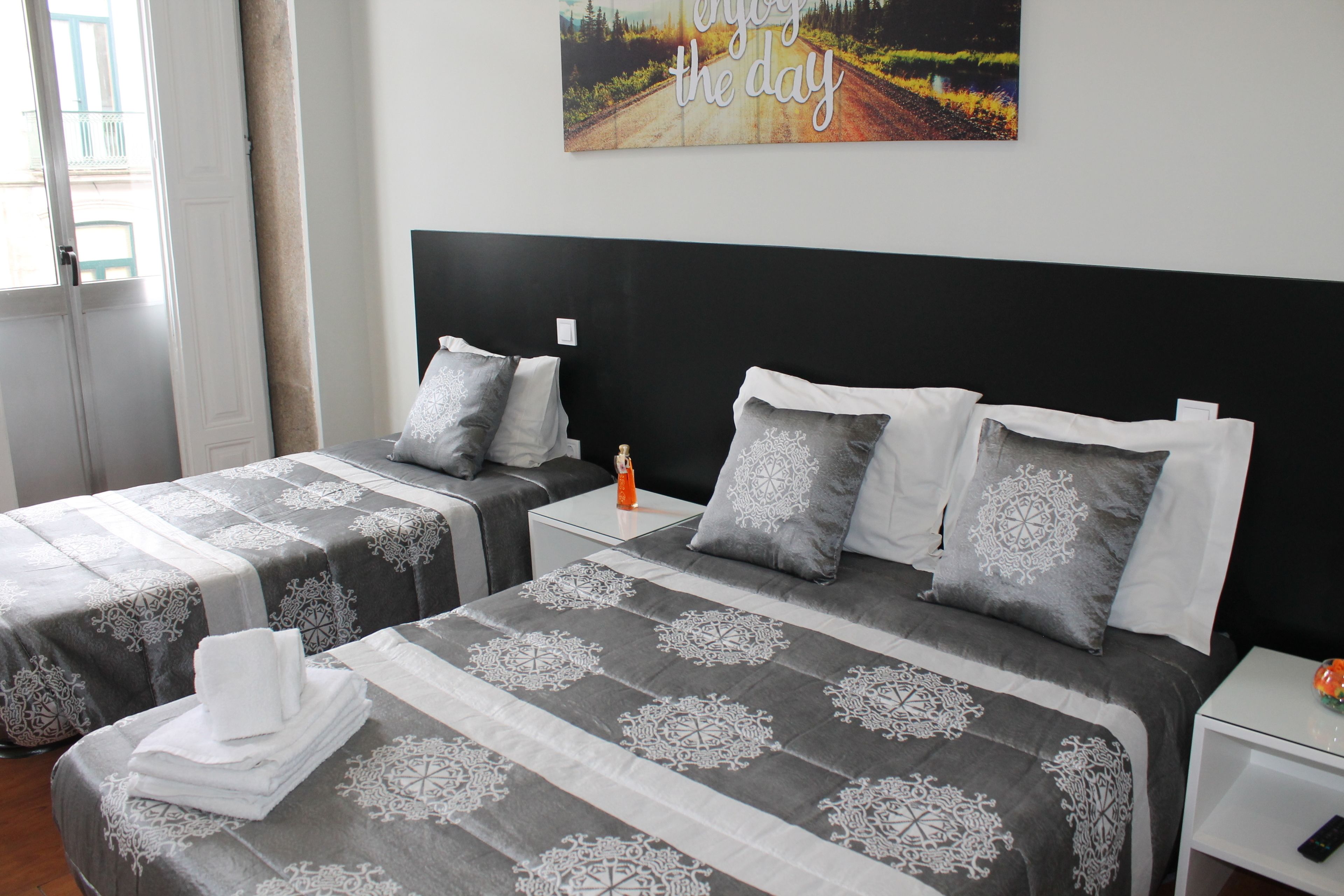 Una habitación de hotel con dos camas, cada una con una colcha de diseño gris y blanco, almohadas blancas y una mesita de noche con un control remoto.