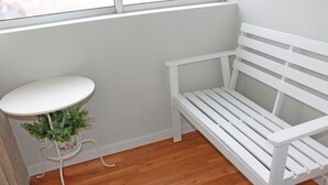 A white bench and a white table with a plant in a corner of a room with wooden flooring. - Lunar Guest House (Porto)