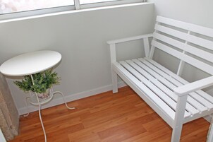 Um banco branco e uma mesa branca com uma planta num canto de um quarto com soalho de madeira.