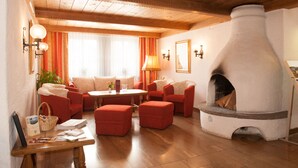 A cozy living room with wooden beams, red upholstered furniture, a fireplace, and a table with various items. - Aktiv- und Wellnesshotel Seeblick (Bad Endorf)